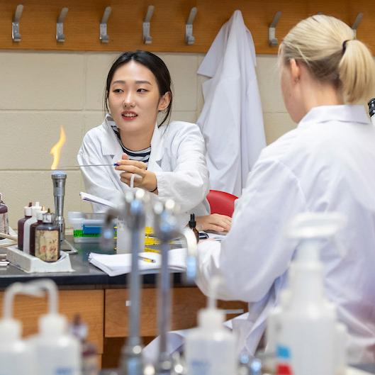 Two female students in white lab coats working in a science lab.
